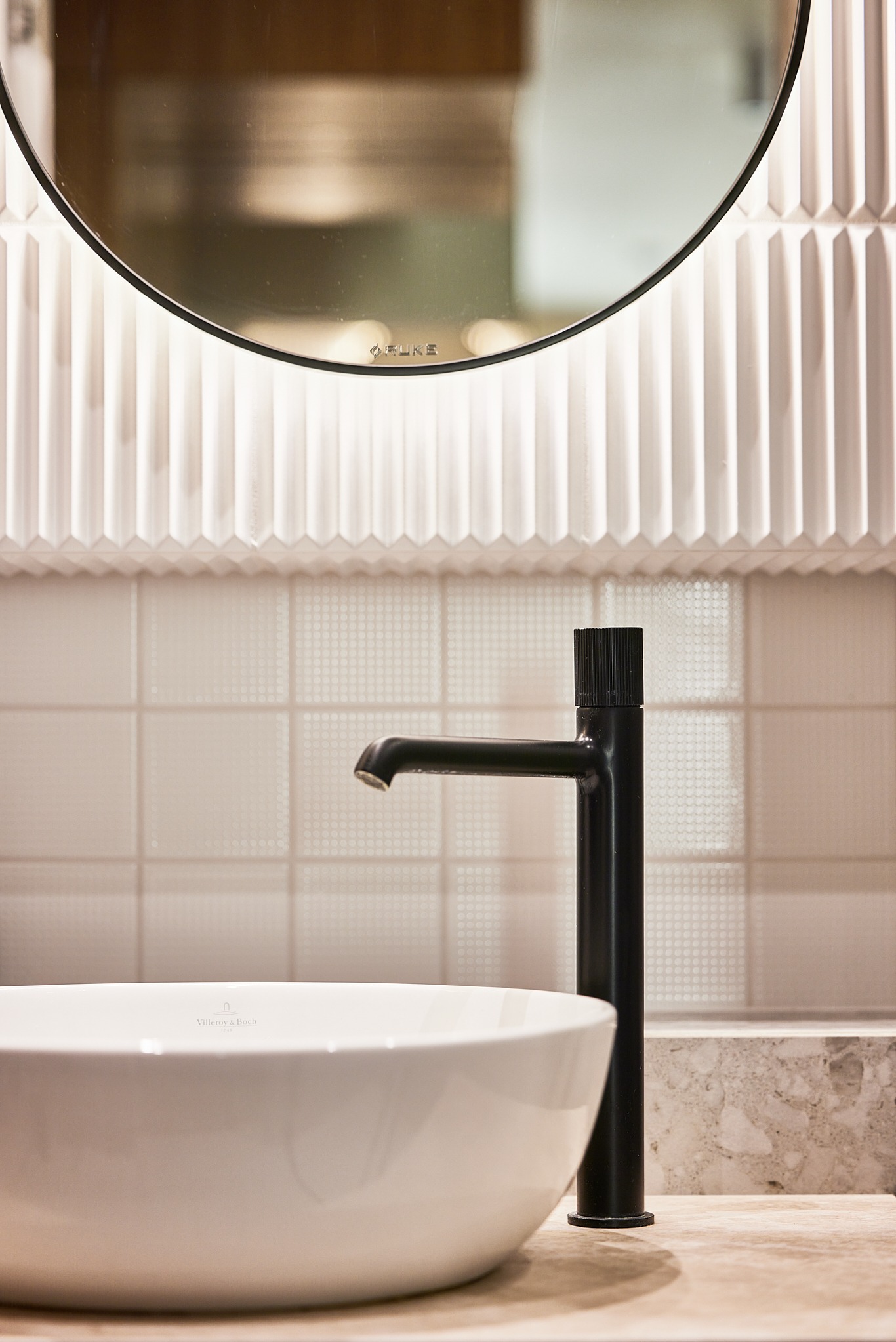 Nowoczesna łazienka z okrągłym lustrem z podświetleniem LED i czarną armaturą. Umywalka marki Villeroy & Boch. Minimalistyczny design i eleganckie wykończenie.