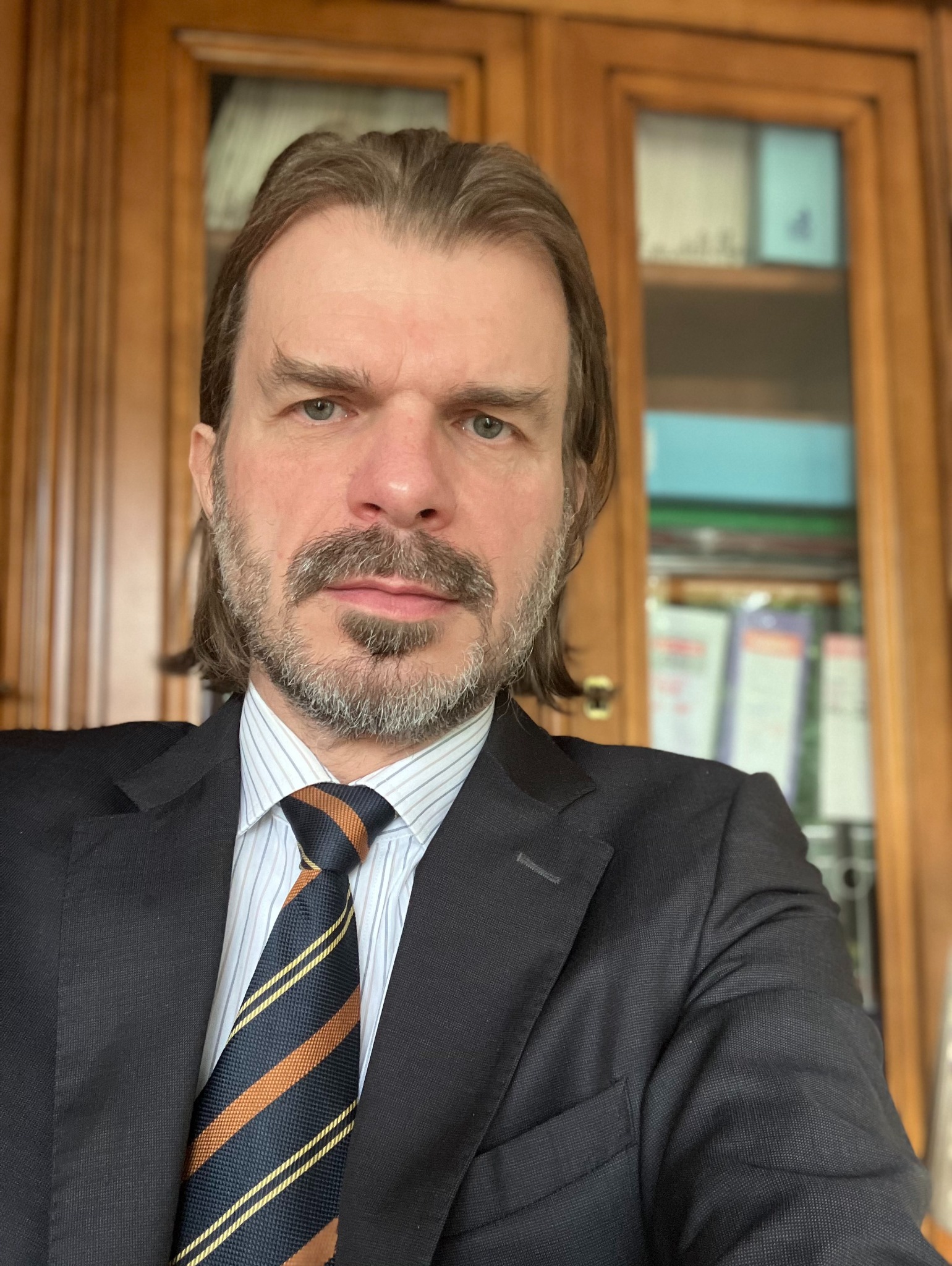 Portret mężczyzny w garniturze i krawacie w paski, na tle drewnianego regału z segregatorami