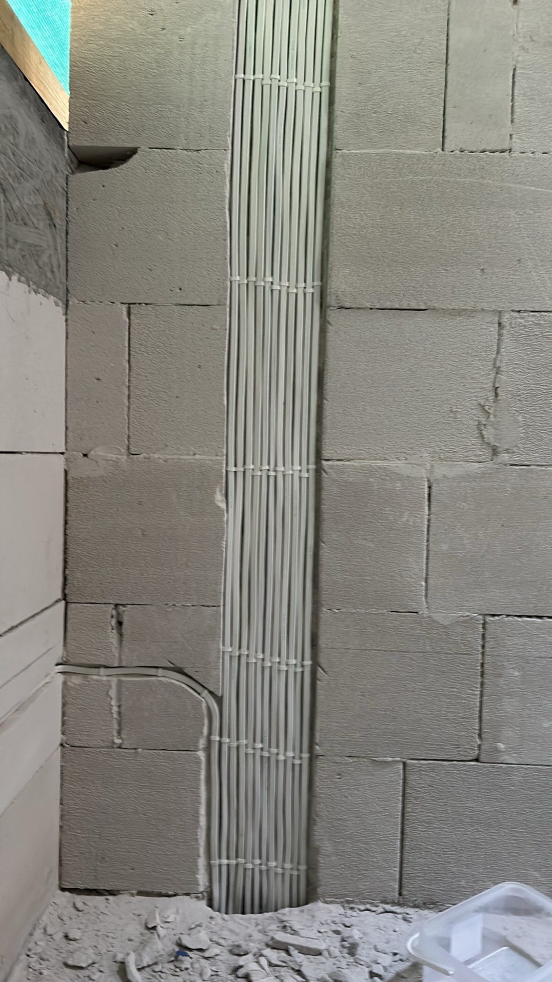 Białe kable elektryczne ułożone pionowo w wyżłobieniu ściany z bloczków betonowych, zabezpieczone opaskami zaciskowymi.