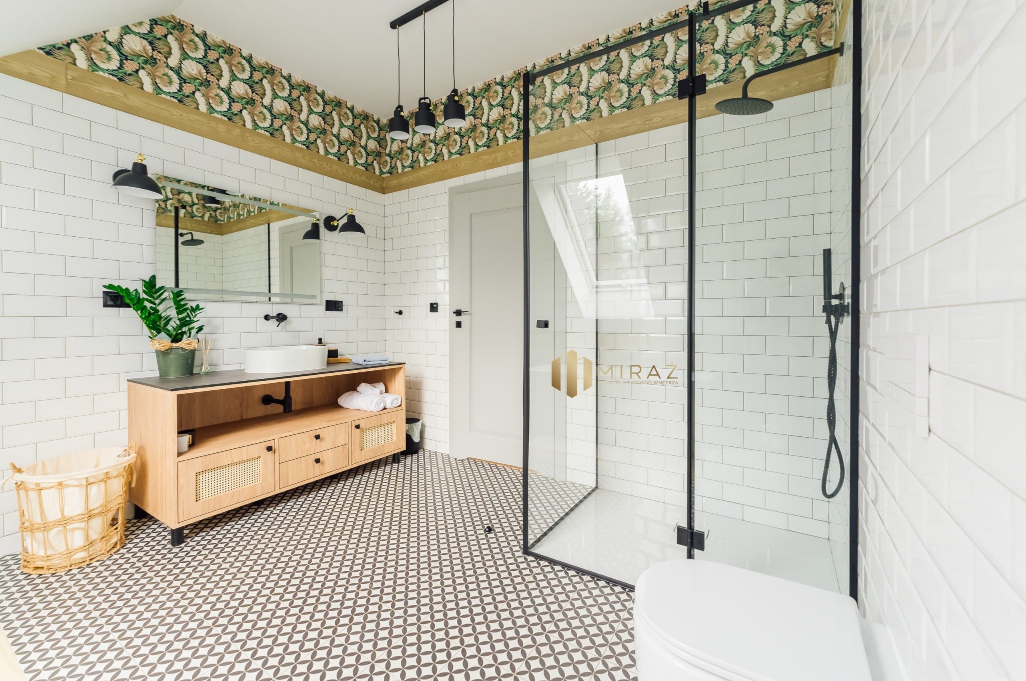 Nowoczesna łazienka z kabiną prysznicową ze szklanymi ścianami w czarnych ramach, białe płytki imitujące cegłę, wzorzysta tapeta na suficie, drewniana szafka pod umywalką i geometryczna podłoga.