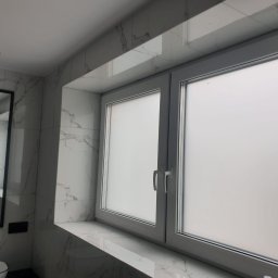 Marci Marcin - Nowoczesna łazienka z marmurowymi płytkami, białymi oknami z matową szybą i czarnym lustrem wiszącym nad toaletą.