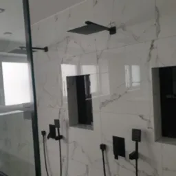 Nowoczesna łazienka z kabiną prysznicową typu walk-in, białe płytki imitujące marmur i czarna armatura: deszczownica, bateria podtynkowa, wnęki z czarnym tłem.