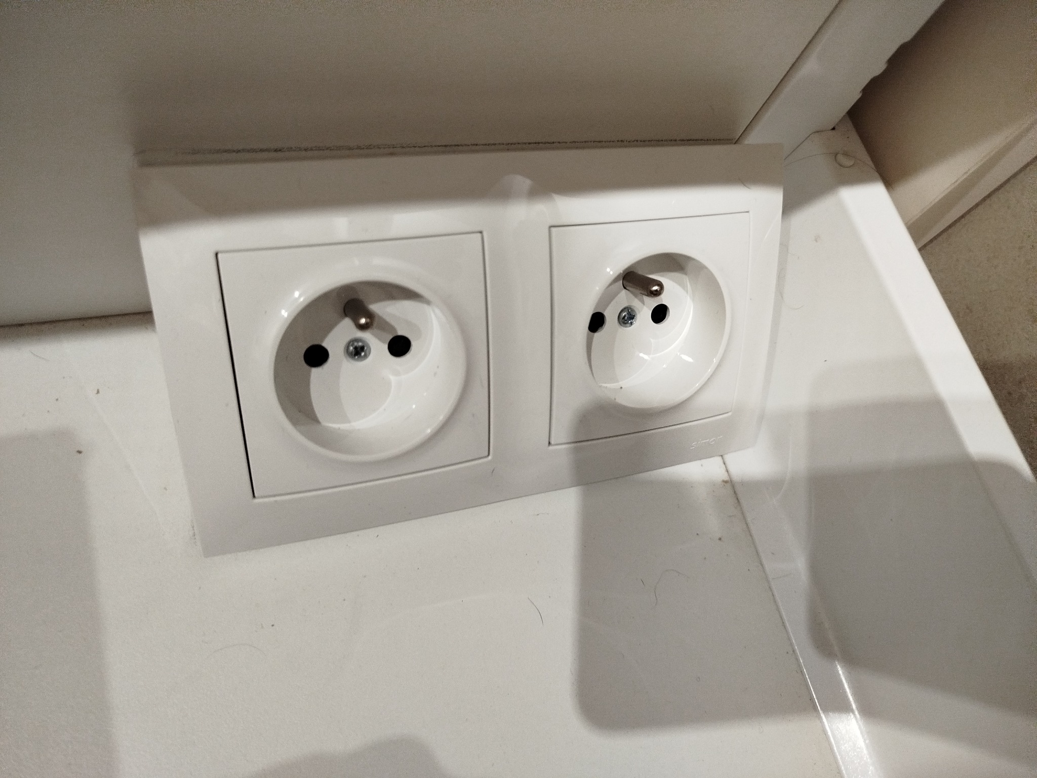 Zamontowane, podwójne gniazdko elektryczne w kolorze białym, widoczne na białej ścianie w mieszkaniu w Łodzi.