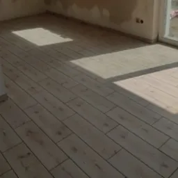 Ułożona podłoga z paneli imitujących drewno w pomieszczeniu w Krosno Odrzańskie, widoczne fragmenty ściany z niedokończonymi pracami, oświetlona wpadającym światłem słonecznym.