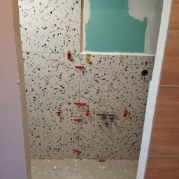 REMO DESIGN - Układanie płytek lastryko w łazience z użyciem klipsów poziomujących. Widoczne fragmenty instalacji wodnej i pomalowana ściana. Prace glazurnicze w toku.