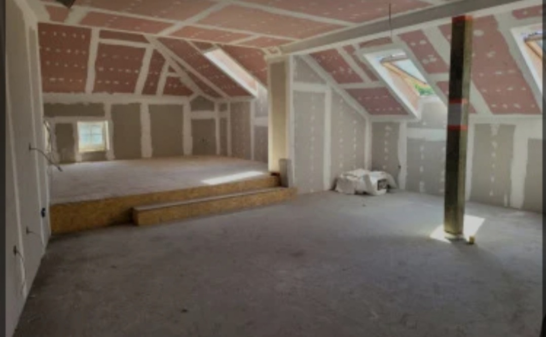 Poddasze w trakcie prac wykończeniowych: zamontowane płyty karton-gips na skośnym suficie z oknami dachowymi i ścianach, widoczne fragmenty konstrukcji drewnianej, podwyższenie podłogi z płyty OSB.