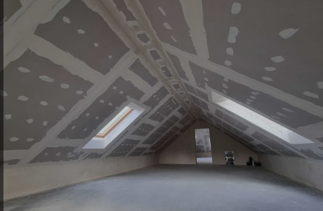 Poddasze z oknami dachowymi w trakcie wykańczania płytami karton-gips, widoczne łączenia zaszpachlowane, przygotowane do dalszych prac wykończeniowych.