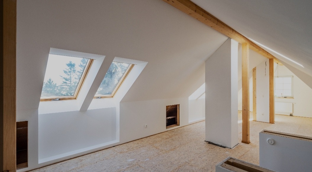 Poddasze po remoncie z dwoma oknami dachowymi, drewnianymi belkami konstrukcyjnymi i podłogą z płyt OSB, widoczne przygotowania do dalszych prac wykończeniowych.