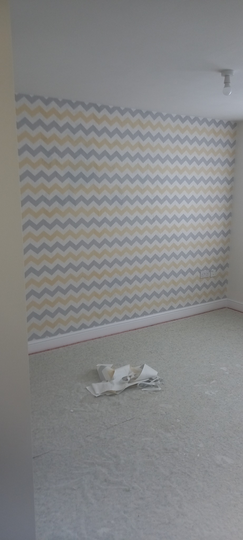 Pokój w trakcie tapetowania w Ostrowie Wielkopolskim, widoczna ściana z wzorem w zygzaki, resztki tapety na podłodze.