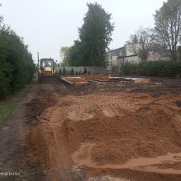 Marcin Zagłoba Usługi Budowlane - Żółta ładowarka czołowa na placu budowy, widoczne wykopane fundamenty i pracownik z łopatą, w tle budynek i drzewa.