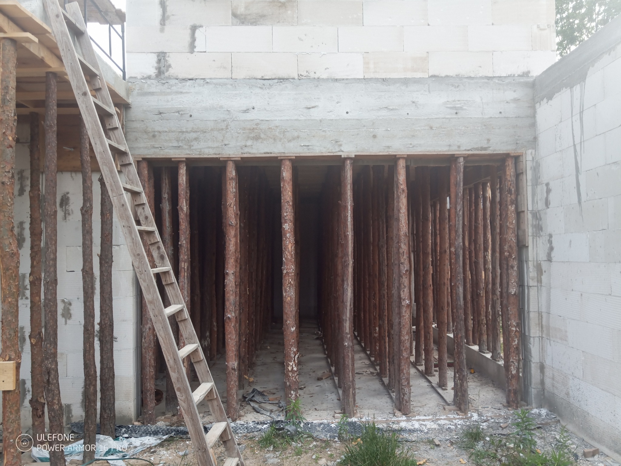 Ściana z betonu komórkowego z drewnianymi stemplami podtrzymującymi strop, widoczna drewniana drabina oparta o ścianę.