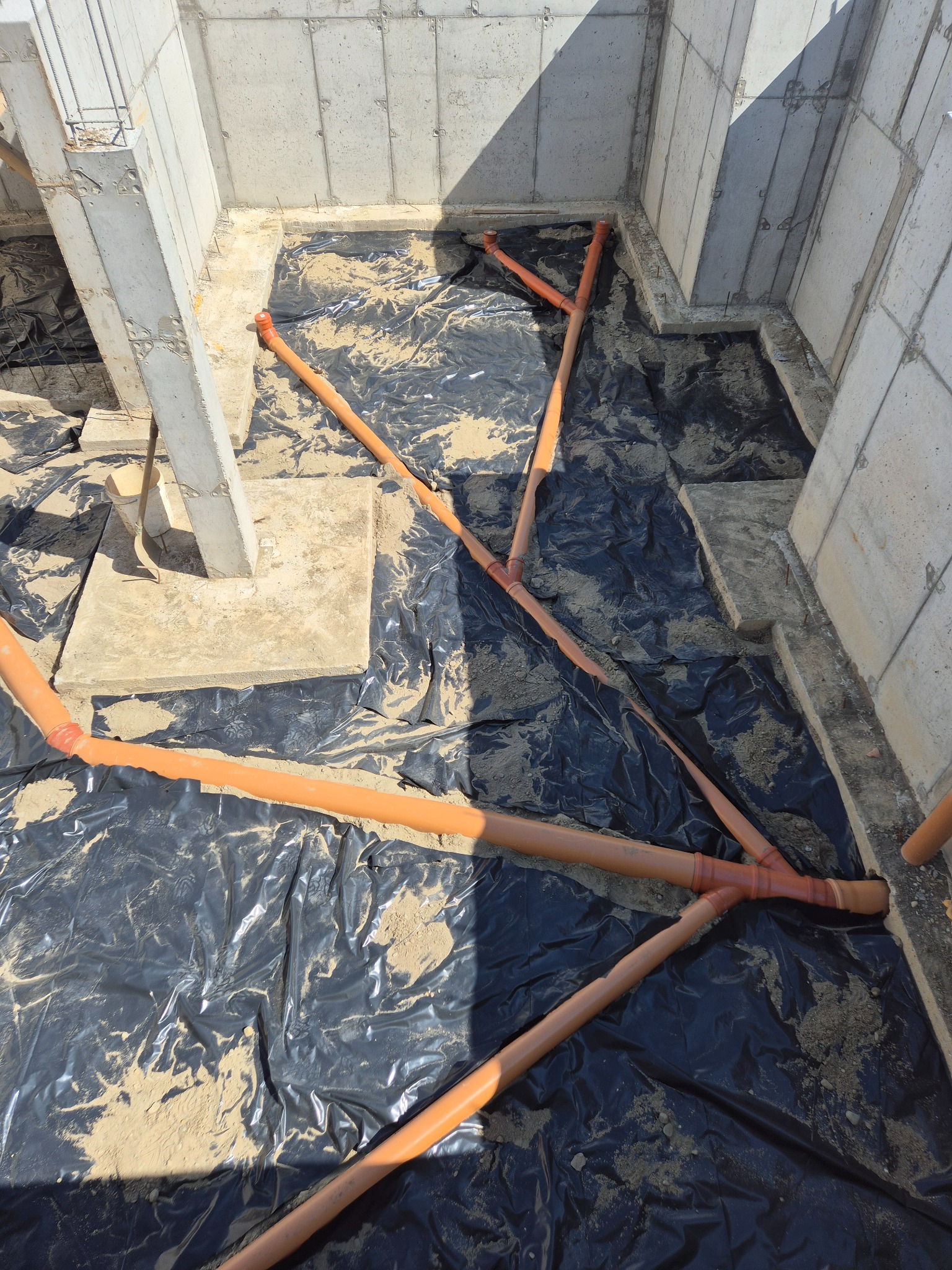 Przygotowanie fundamentów w Białym Dunajcu: widok na betonowe ściany fundamentowe, czarną folię izolacyjną i pomarańczowe rury drenażowe ułożone na piasku.