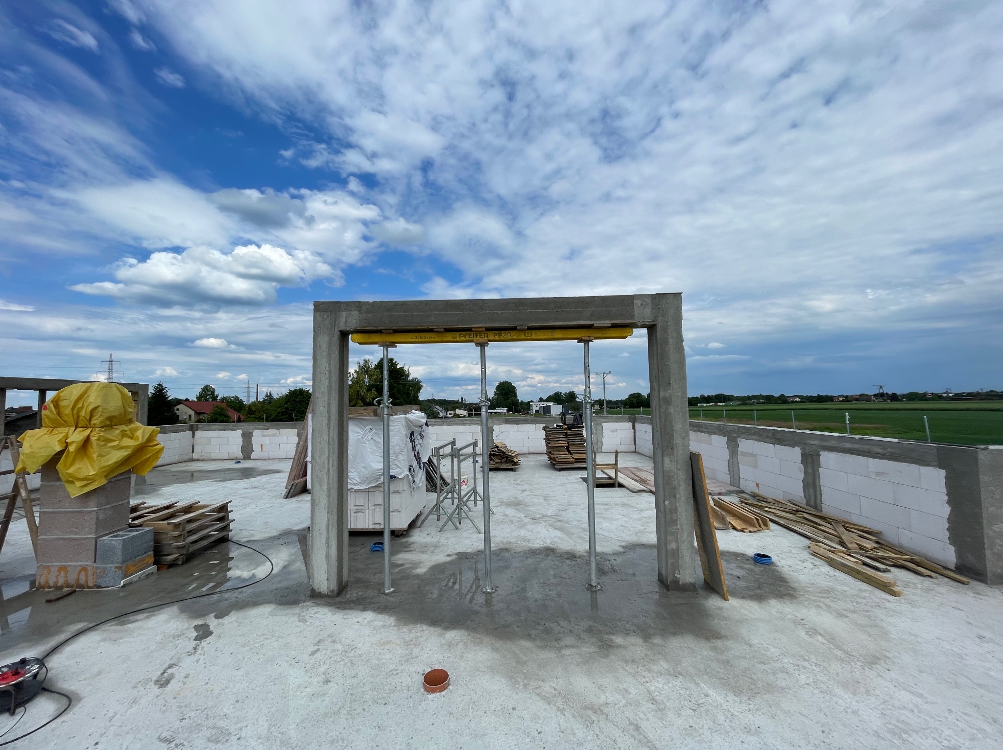 Budowa domu z betonu komórkowego Ytong w miejscowości Łąka, widok na wznoszoną konstrukcję stropu z szalunkami i stemplami, w tle błękitne niebo z obłokami.