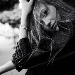 Patrycja Błajdo Fotografia - Czarno-białe portretowe ujęcie kobiety z długimi włosami, opierającej głowę na dłoni, ubranej w skórzaną kurtkę z widoczną klamrą, z zamyślonym wyrazem twarzy.