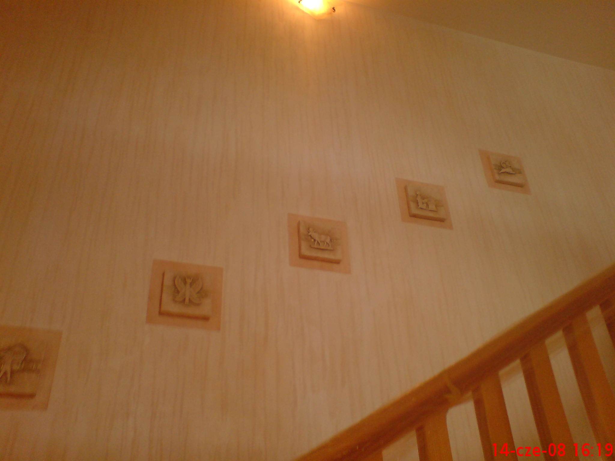 Ściana pokryta dekoracyjną fakturą z motywami zwierzęcymi w kwadratowych ramach, widoczna fragment drewnianej balustrady schodów.
