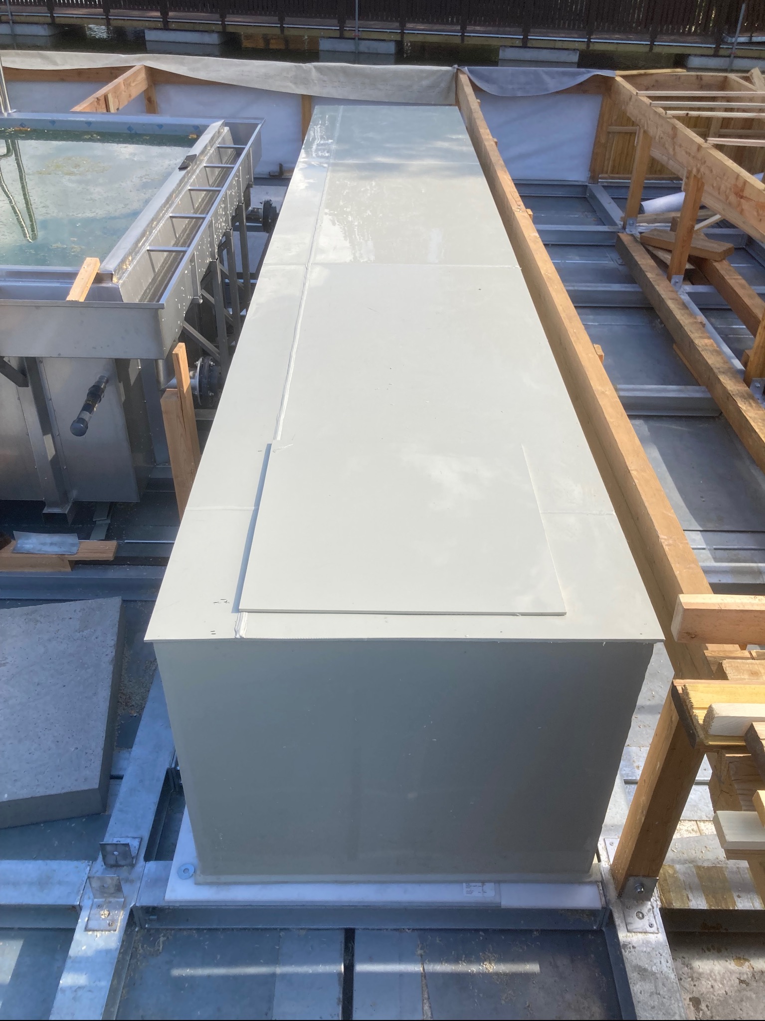 Etap budowy długiego, wąskiego zbiornika, prawdopodobnie elementu składowego basenu, z widoczną drewnianą konstrukcją wsporczą i metalowymi elementami montażowymi.