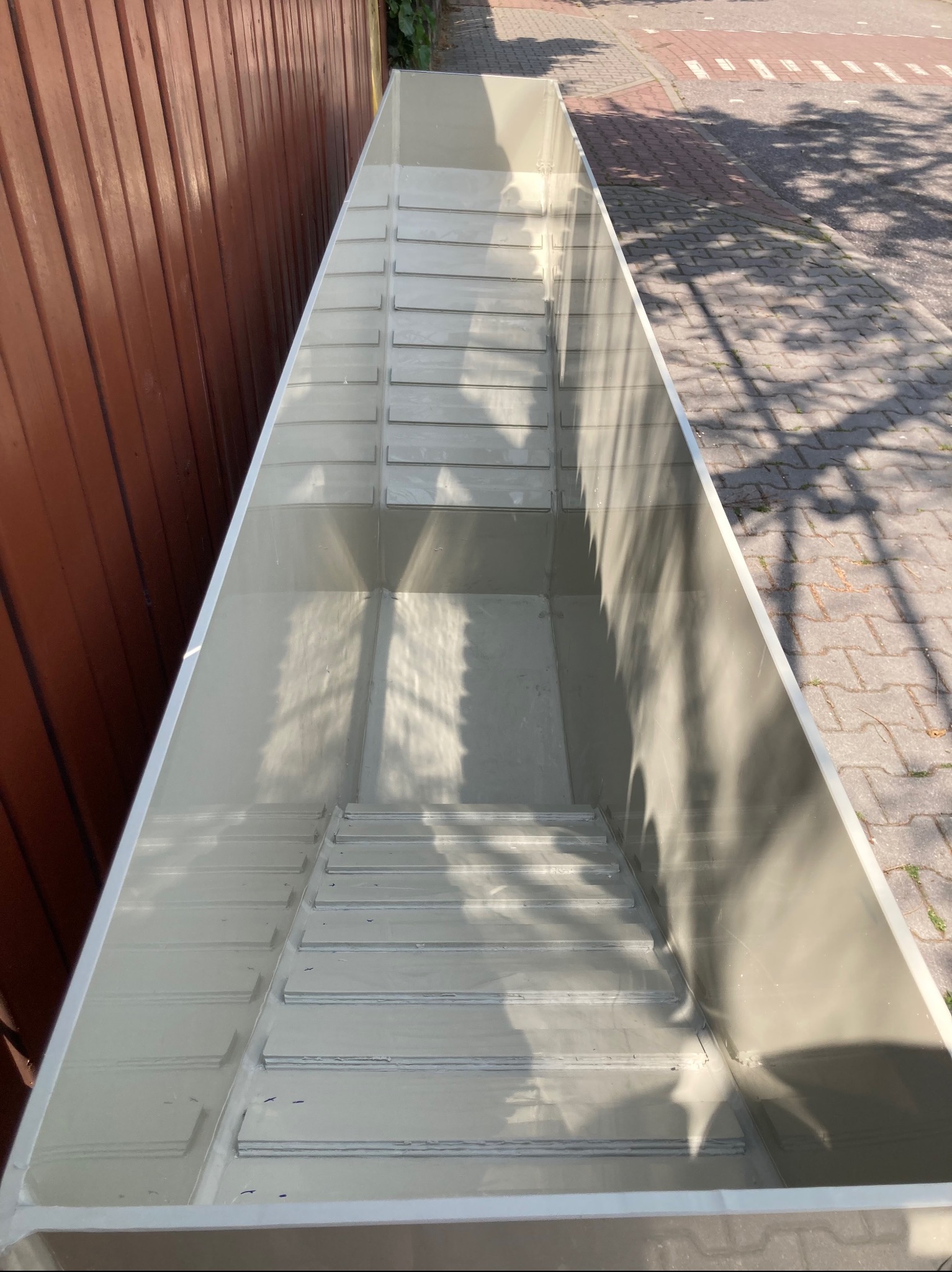 Nowy, pusty, prostokątny zbiornik z tworzywa sztucznego, prawdopodobnie do budowy oczka wodnego lub basenu, sfotografowany z góry w Warszawie. Widoczna faktura wewnętrznych ścianek i cień drzewa...