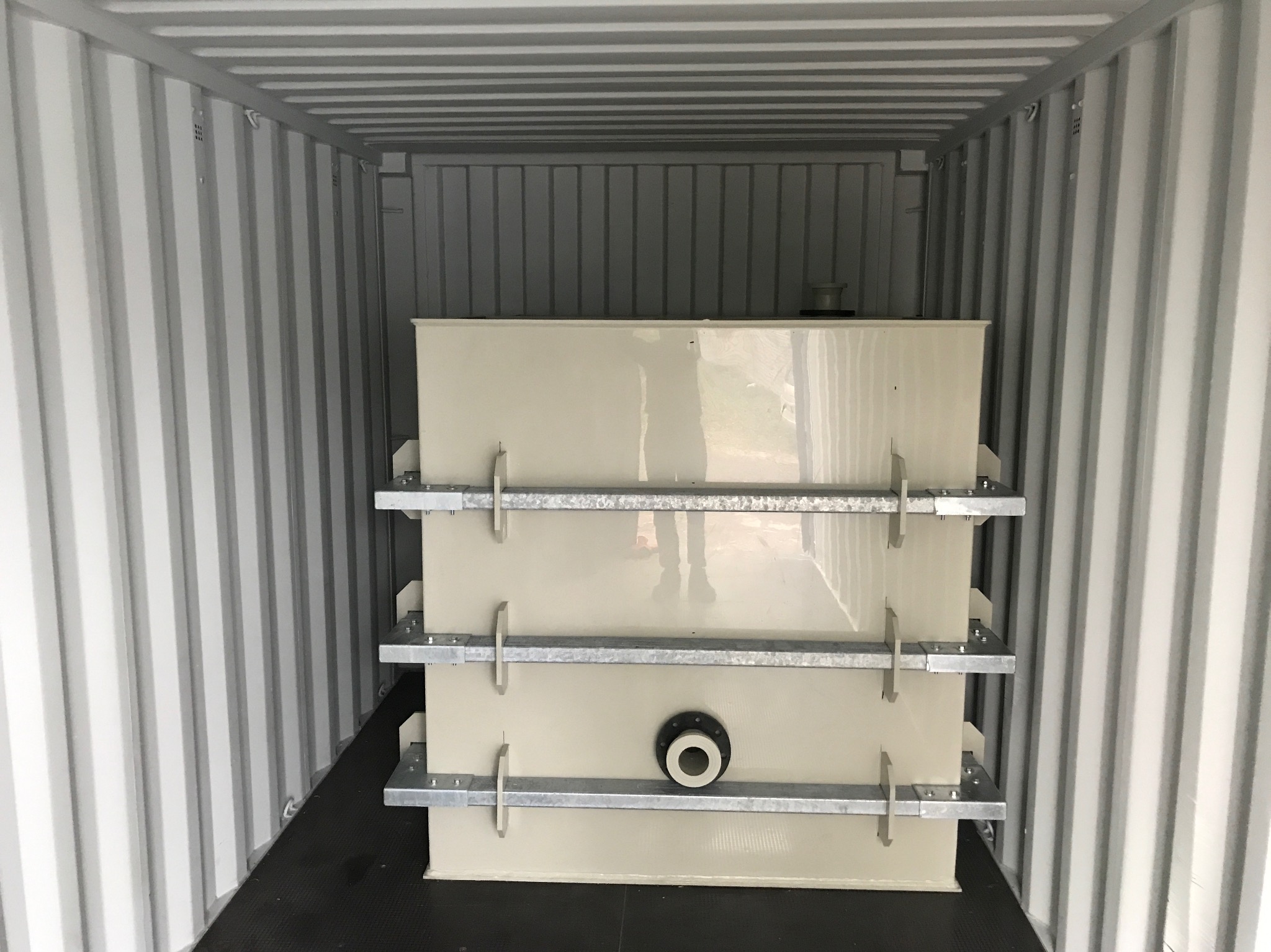 Zbiornik z metalowymi wzmocnieniami w kontenerze transportowym, widoczny otwór przyłączeniowy.