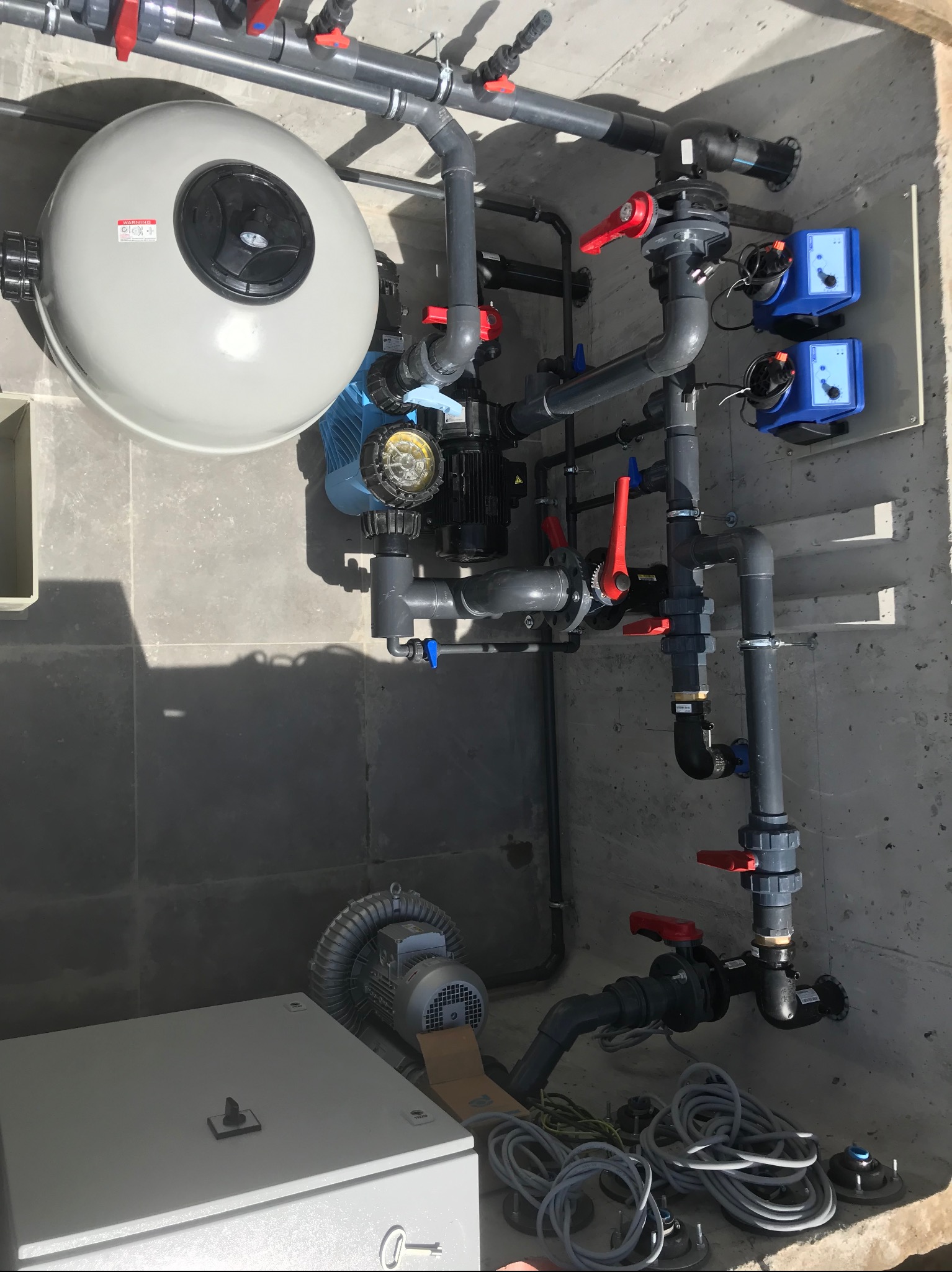 Kompletna instalacja filtracyjna z pompami dozującymi i zbiornikiem ciśnieniowym w pomieszczeniu technicznym, widok z góry.