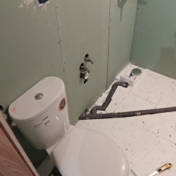 Zbigniew Niewiadomy - Niedokończona łazienka: biała toaleta z naklejką producenta, częściowo położone płytki podłogowe z widocznym nożem do cięcia, ściany wyłożone płytami gipsowo-kartonowymi z widocznymi instalacjami...