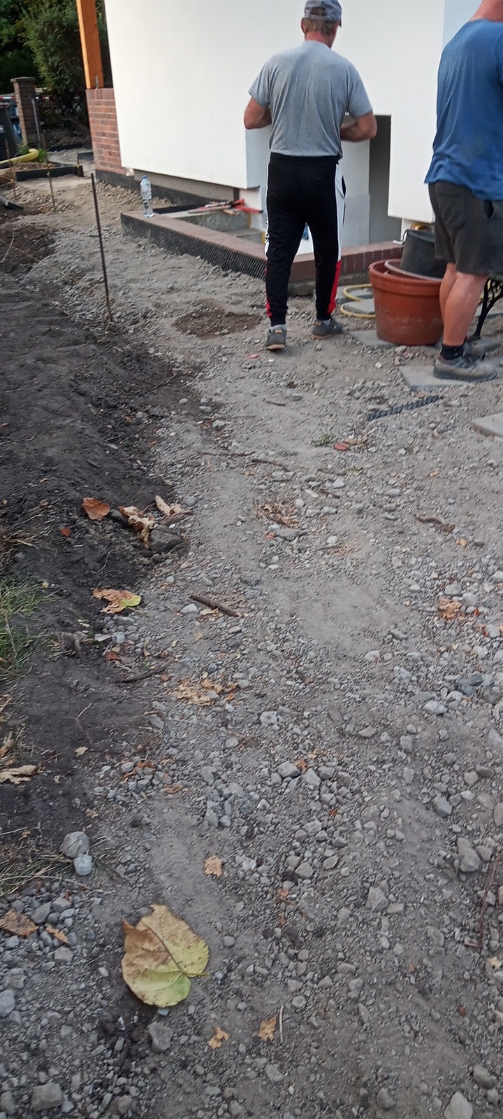 Przygotowanie podłoża pod kostkę: wyrównywanie terenu przy budynku, widoczne narzędzia i materiały budowlane.