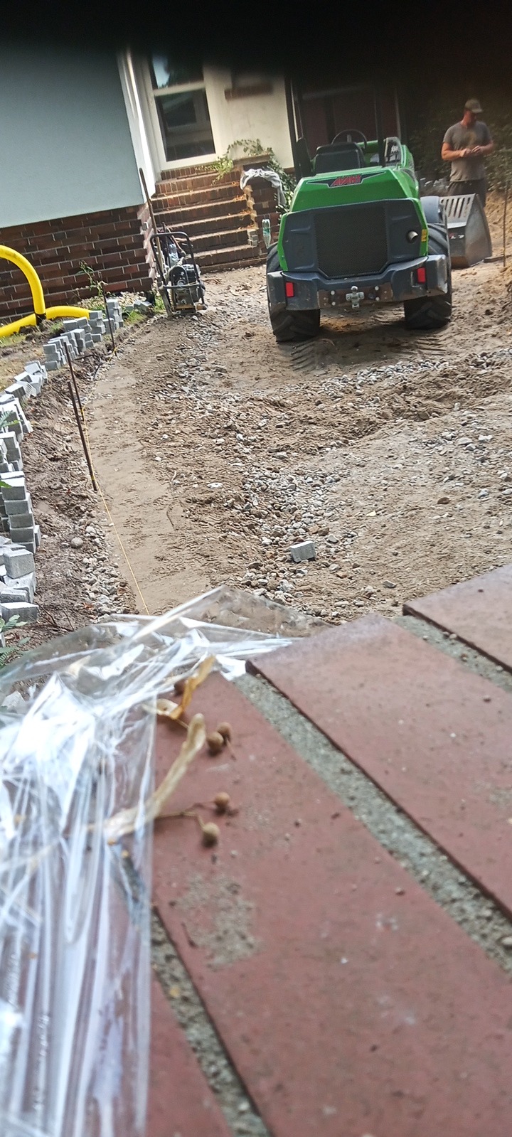 Przygotowanie podłoża pod ścieżkę z kostki: widoczny wykop, ustawione krawężniki, ubijarka i minikoparka, w tle pracownik.