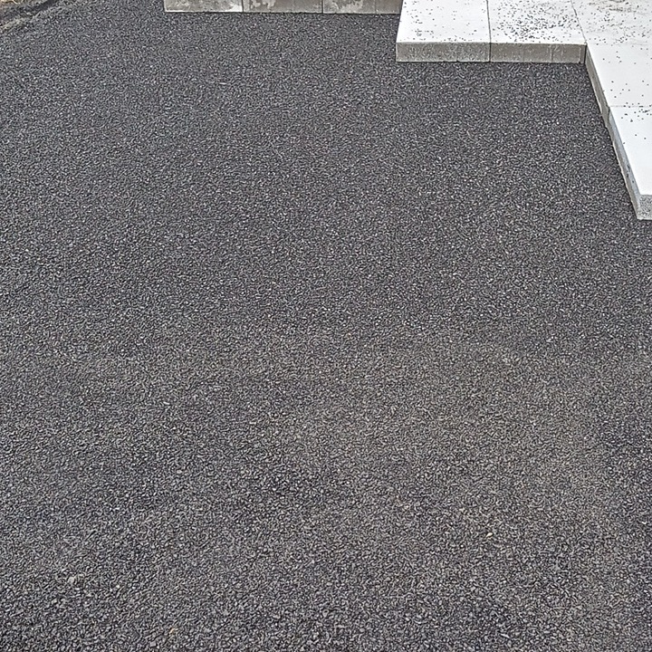 Podłoże z drobnego grysu pod kostkę brukową, z częściowo ułożonymi jasnoszarymi kostkami na obrzeżach, widok z góry.