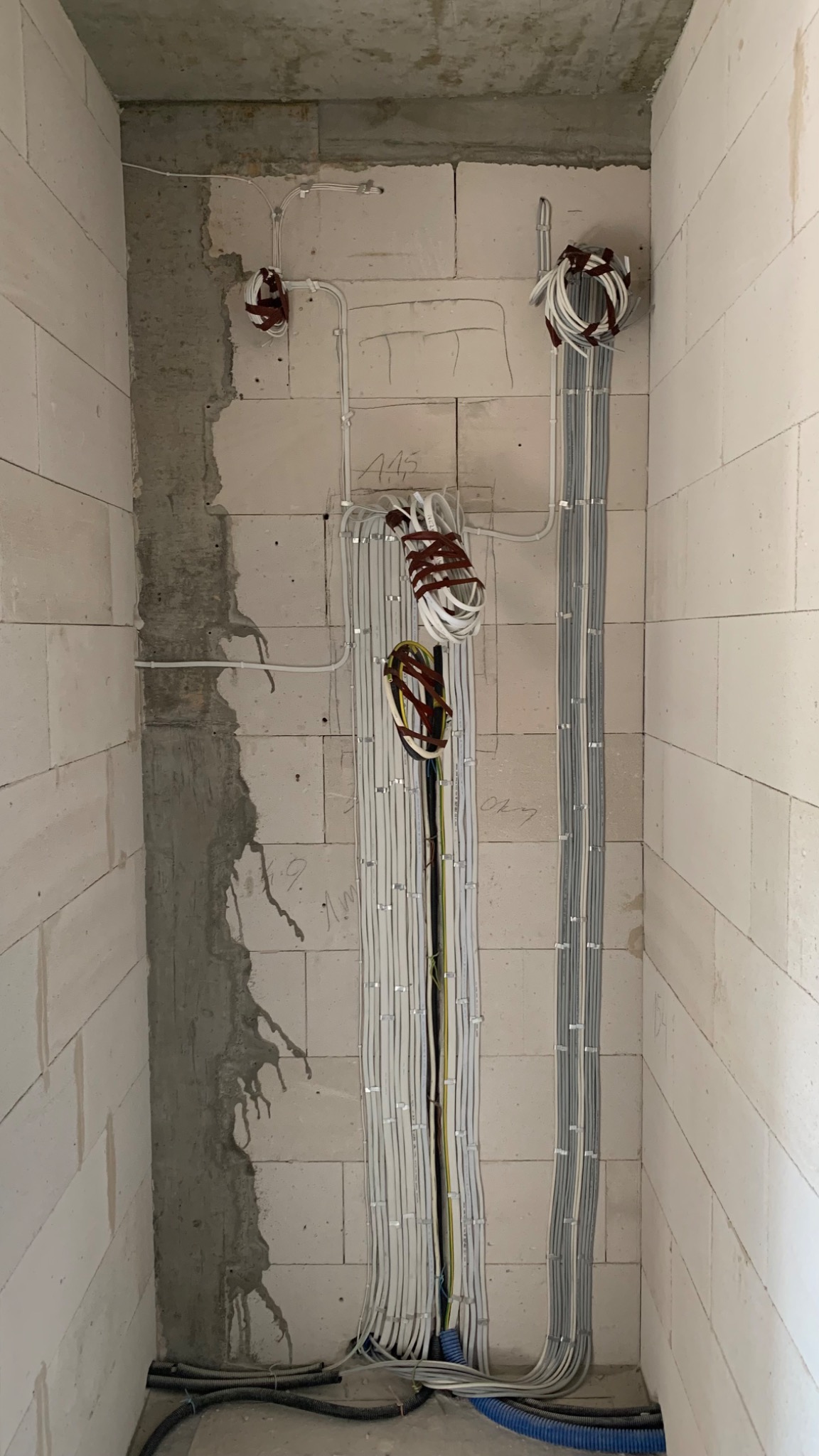 Wewnętrzna instalacja elektryczna w surowym wnętrzu: kable ułożone pionowo wzdłuż ściany z betonu komórkowego, zabezpieczone uchwytami. Widoczne przewody w peszlach przy podłodze.