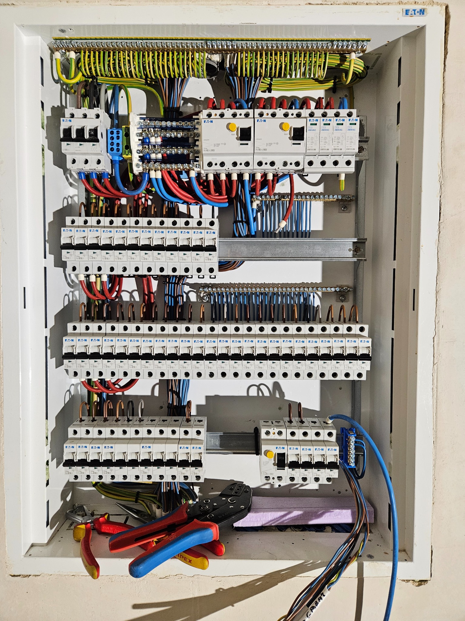 Rozdzielnica elektryczna marki Eaton z licznymi zabezpieczeniami, okablowaniem w kolorach, narzędzia monterskie w dolnej części kadru. Widok z góry.