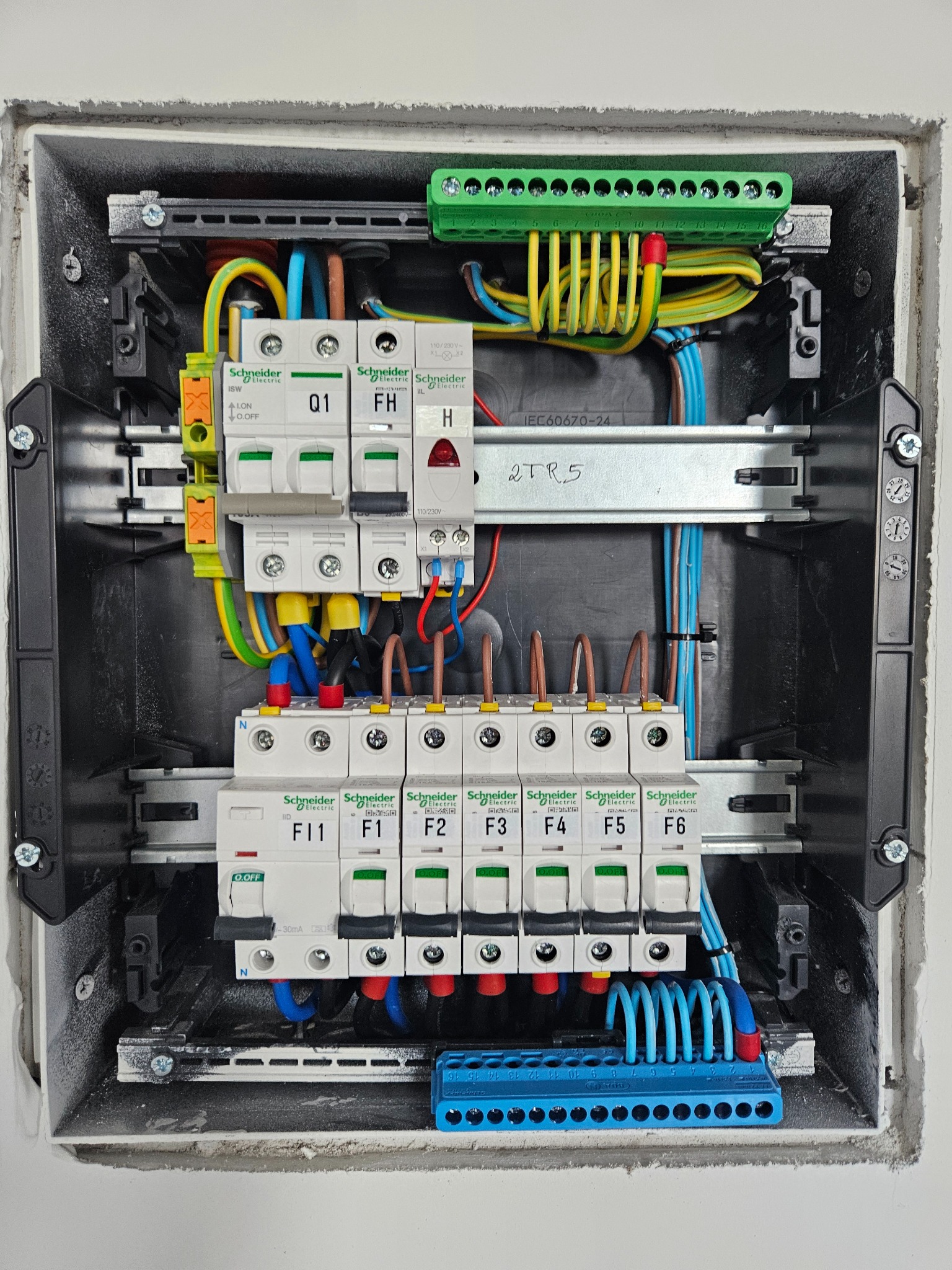Rozdzielnica elektryczna Schneider Electric w szarej obudowie, widoczne bezpieczniki, przewody w różnych kolorach i listwy zaciskowe. Instalacja w trakcie montażu.