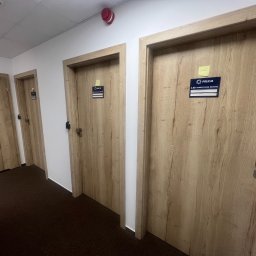 Mivol - Korytarz z trzema drewnianymi drzwiami z tabliczkami informacyjnymi 'Policja' i numerami pomieszczeń, widoczne brązowe wykładziny podłogowe.