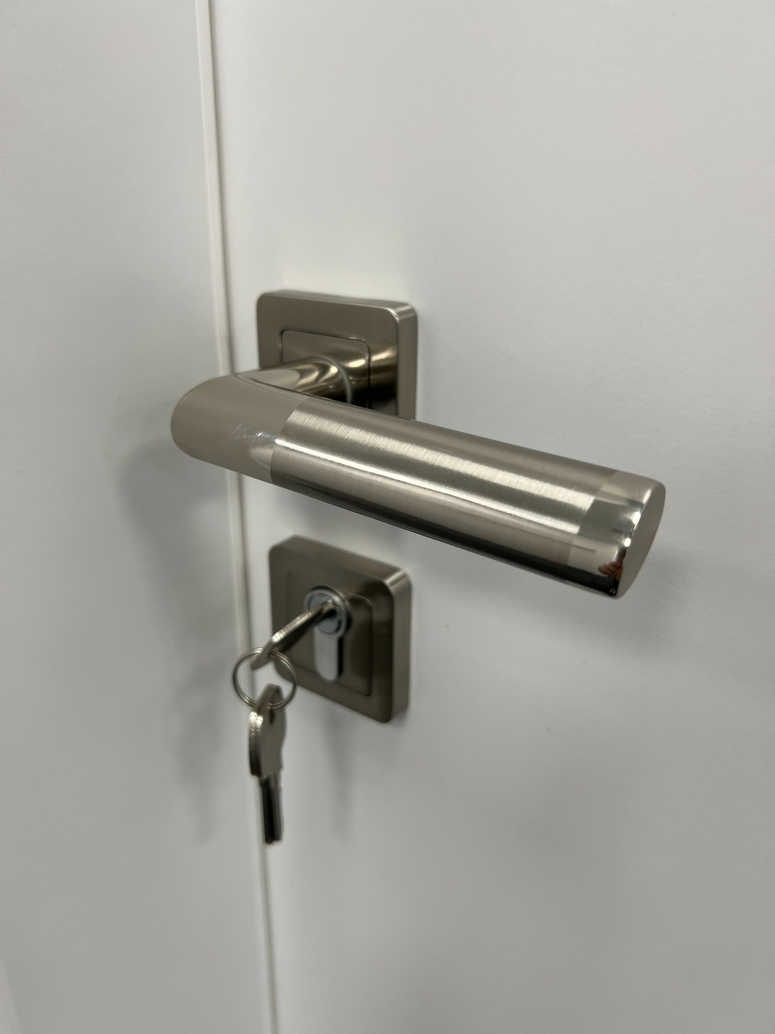 Szczegółowe ujęcie srebrnej klamki i zamka z kluczem w białych drzwiach wewnętrznych.