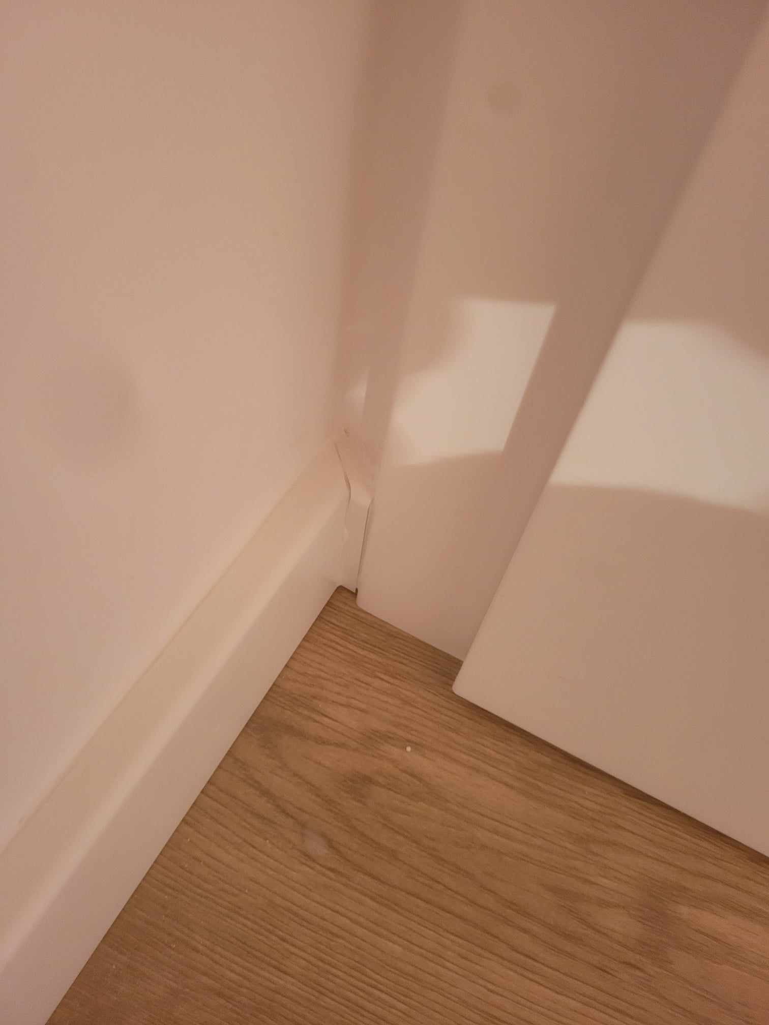 Fragment rogu pokoju po ułożeniu paneli podłogowych, widoczna listwa przypodłogowa i szczelina między nią a ścianą.