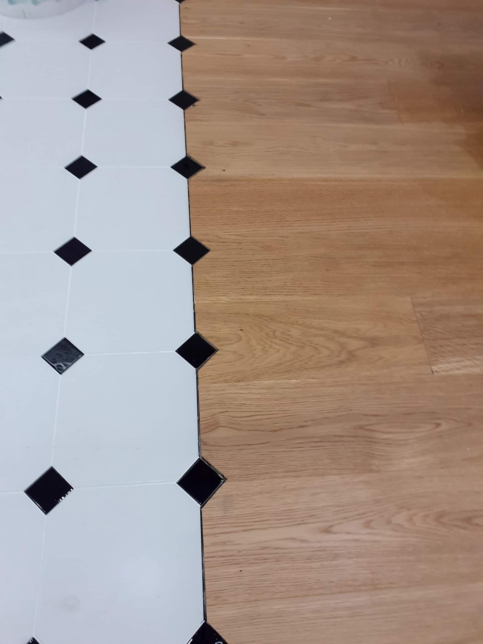 Połączenie białych płytek z czarnymi rombami i drewnianych paneli podłogowych w Smólniku, ukazujące etap prac wykończeniowych.