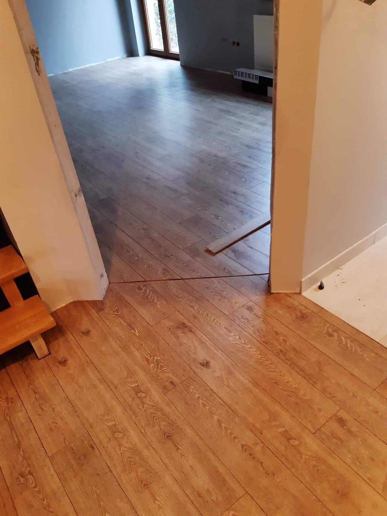 Fragment układania paneli podłogowych z widocznym przejściem między dwoma rodzajami paneli w przejściu między pomieszczeniami, z fragmentem schodów po lewej stronie.