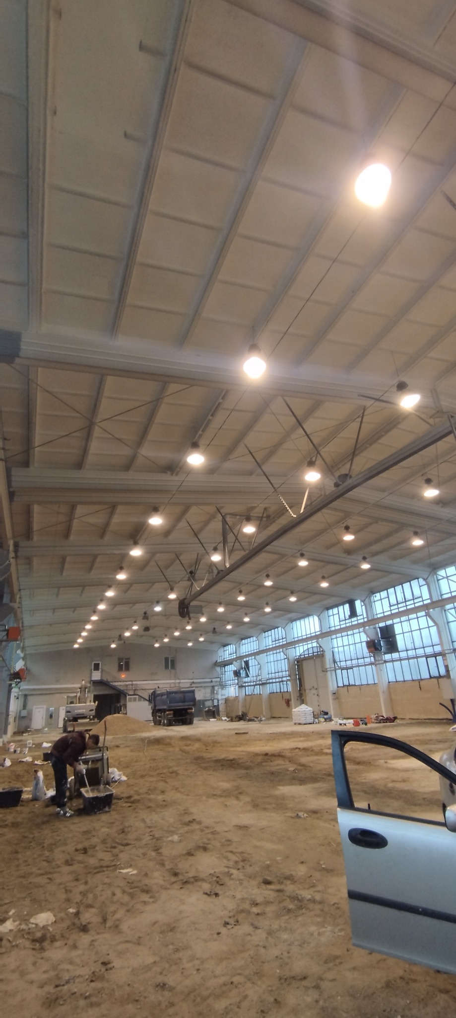 Przygotowanie zaprawy w hali w Warszawie przed pracami wykończeniowymi, widoczny mikser do zaprawy i worki z materiałami, w tle ciężarówka.