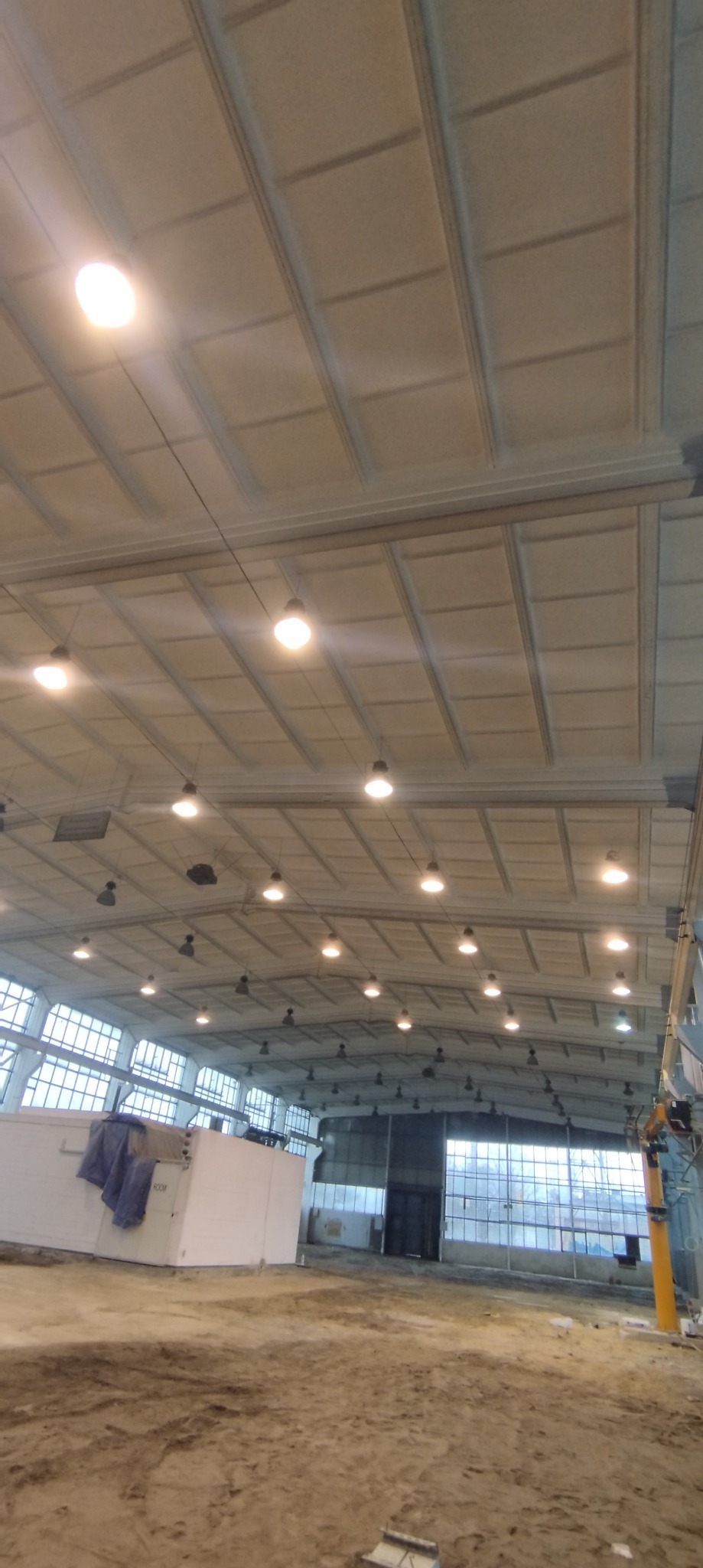 Wnętrze hali przemysłowej w trakcie remontu, z widocznym przygotowanym podłożem i charakterystycznym stropem kasetonowym z oświetleniem.