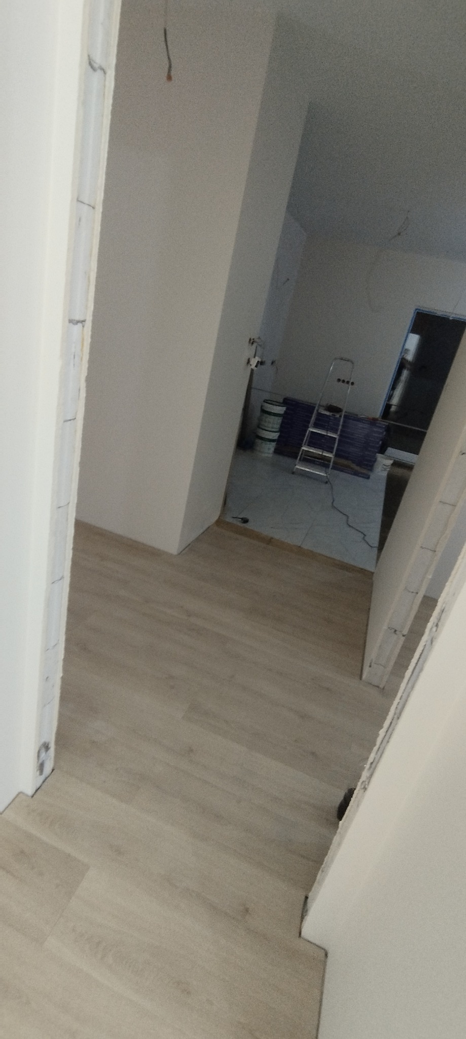 Wnętrze mieszkania w trakcie remontu, widoczne świeżo pomalowane ściany, podłoga, drabina i puszki farby w tle.