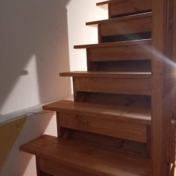 Ewsylwer zakład stolarski - Drewniane schody wewnętrzne z jasnego drewna, widoczne stopnie i fragment poręczy, oświetlone od góry.