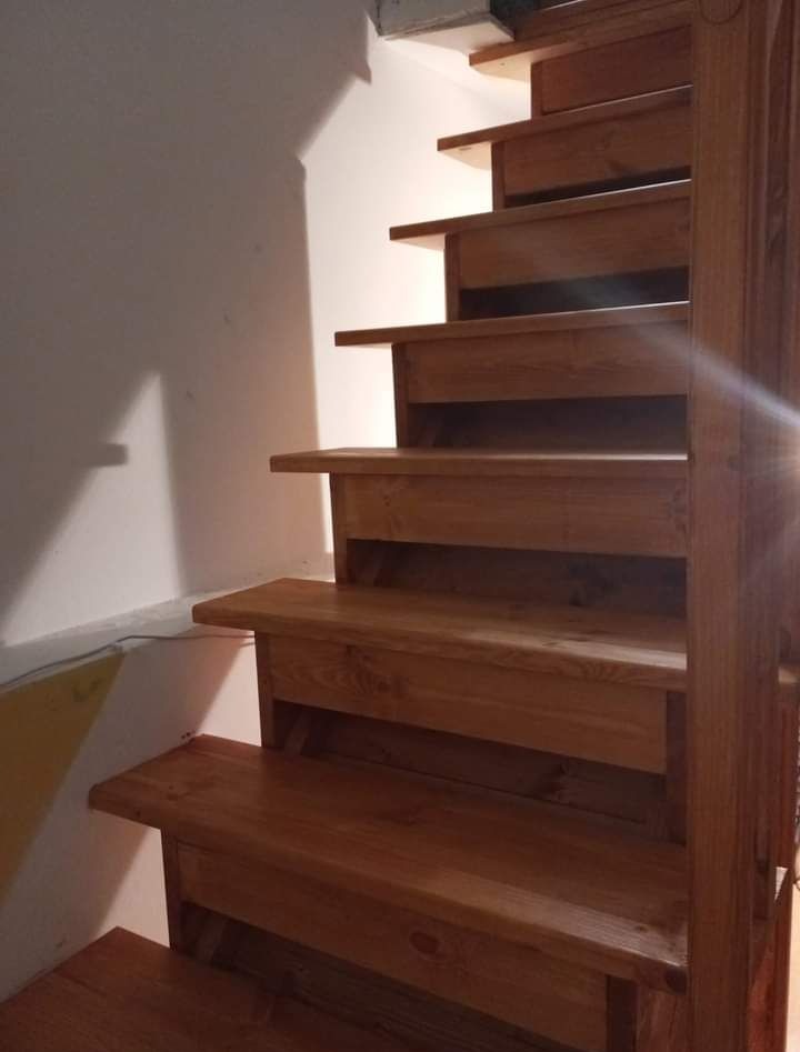 Drewniane schody wewnętrzne z jasnego drewna, widoczne stopnie i fragment poręczy, oświetlone od góry.