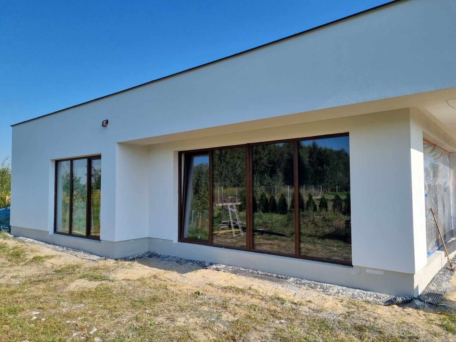 Nowoczesny, parterowy dom z dużymi oknami w Radomiu, elewacja w jasnym kolorze, widoczne prace wykończeniowe przy narożniku budynku.