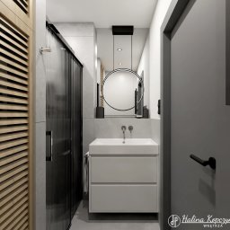 Halina Kopczyńska WNĘTRZA - Trójmiasto i okolice - Nowoczesna łazienka z umywalką nablatową, okrągłym lustrem z podświetleniem LED, kabiną prysznicową z czarnymi prążkowanymi szybami oraz drewnianą szafką z lamelami.