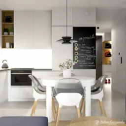 Nowoczesna, jasna kuchnia z białymi meblami, okrągłym stołem i transparentnymi krzesłami. Na ścianie czarna tablica kredowa z menu. W tle widoczny przedpok&oacute;j z p&oacute;łkami.