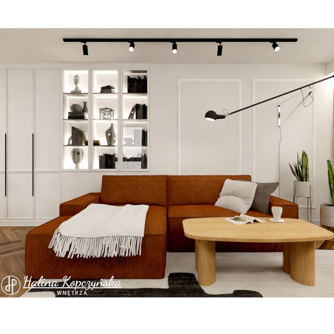 Nowoczesny salon z kordową sofą w kolorze rdzy, drewnianym stolikiem kawowym i oświetleniem szynowym, uzupełniony białymi szafkami z podświetlanymi półkami ekspozycyjnymi.
