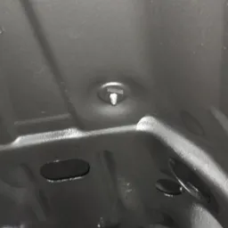 Wnętrze elementu karoserii pojazdu po piaskowaniu, widoczna czysta, szorstka powierzchnia metalu i śruba mocująca.