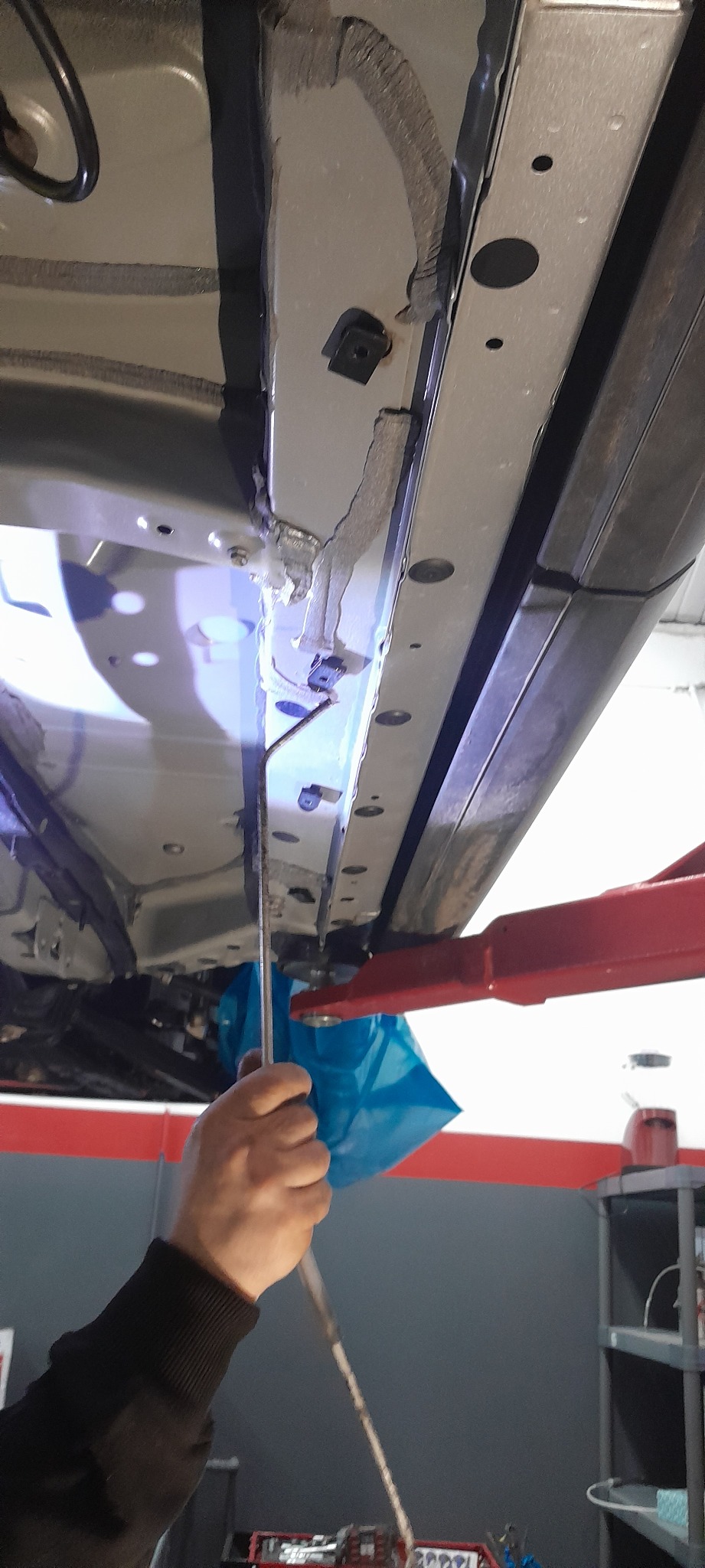 Pracownik warsztatu samochodowego sprawdza podwozie auta na podnośniku, używając narzędzia do inspekcji trudno dostępnych miejsc.