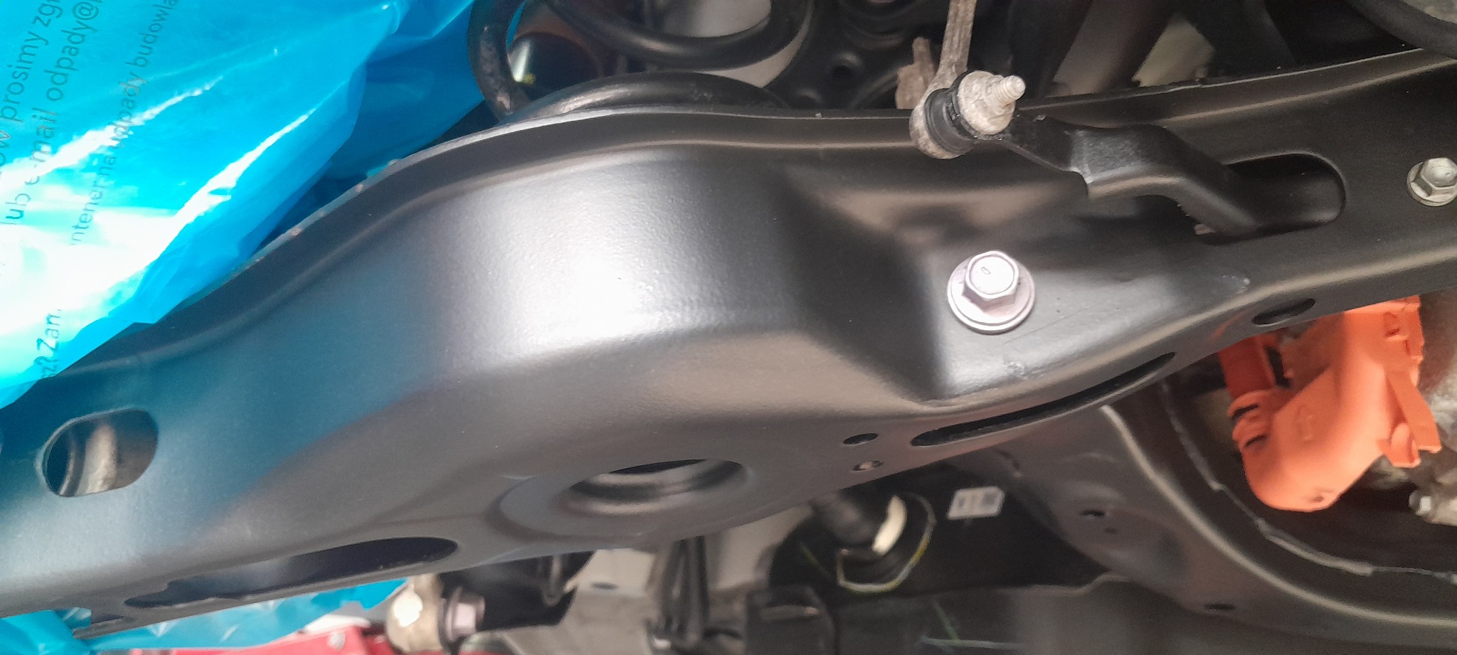 Element zawieszenia pojazdu po zabiegach konserwacyjnych, widoczny świeżo pomalowany element w kolorze czarnym, śruby mocujące oraz fragment pomarańczowej instalacji elektrycznej.