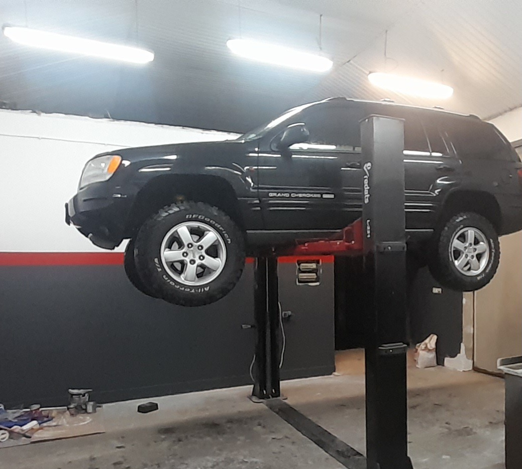 Czarny Jeep Grand Cherokee na podnośniku samochodowym w warsztacie, widoczne opony BFGoodrich All-Terrain T/A.