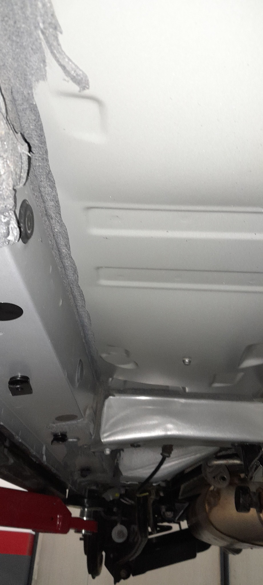 Widok podwozia samochodu na podnośniku, z widoczną warstwą zabezpieczenia antykorozyjnego i elementami zawieszenia.