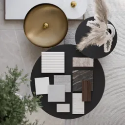 Moodboard z próbkami materiałów wykończeniowych (drewno, marmur, tkaniny) na czarnym stoliku kawowym, uzupełniony o dekoracje: wazon z pampasową trawą, złota misa i abstrakcyjny obraz, widok z góry.
